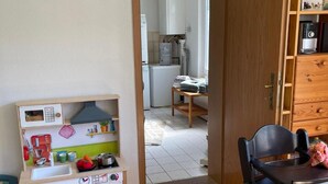 Ein Zimmer mit einer Holz-Spieleküche, einem Esstisch mit Stühlen und einer Holzkabine mit Büchern.