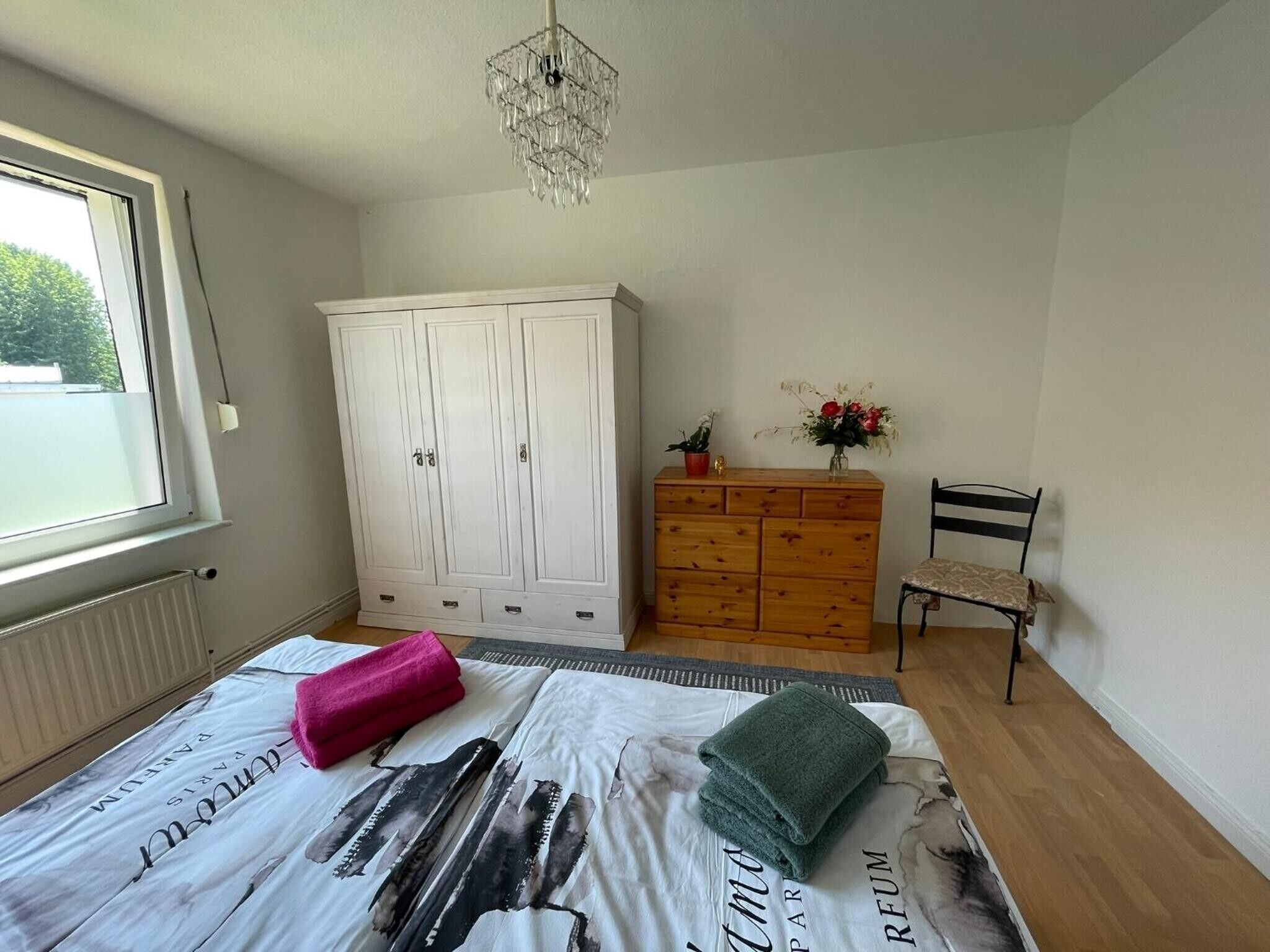 Ein Schlafzimmer mit Bett, Kleiderschrank, Kommode, Stuhl und Fenster.