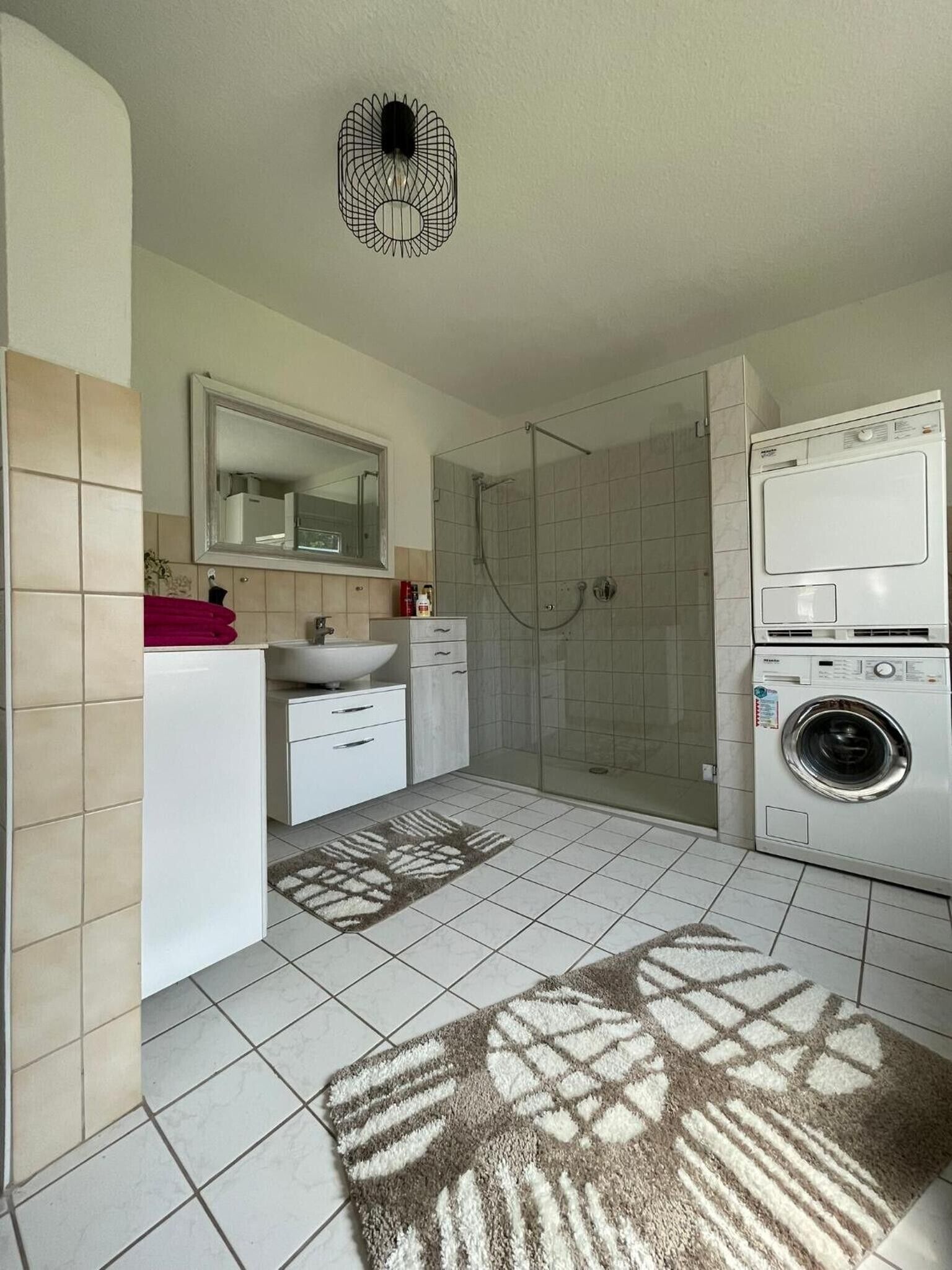 A modern bathroom with a shower, sink, and stacked washer and dryer.