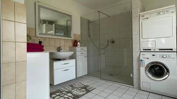 A modern bathroom with a shower, sink, and stacked washer and dryer.