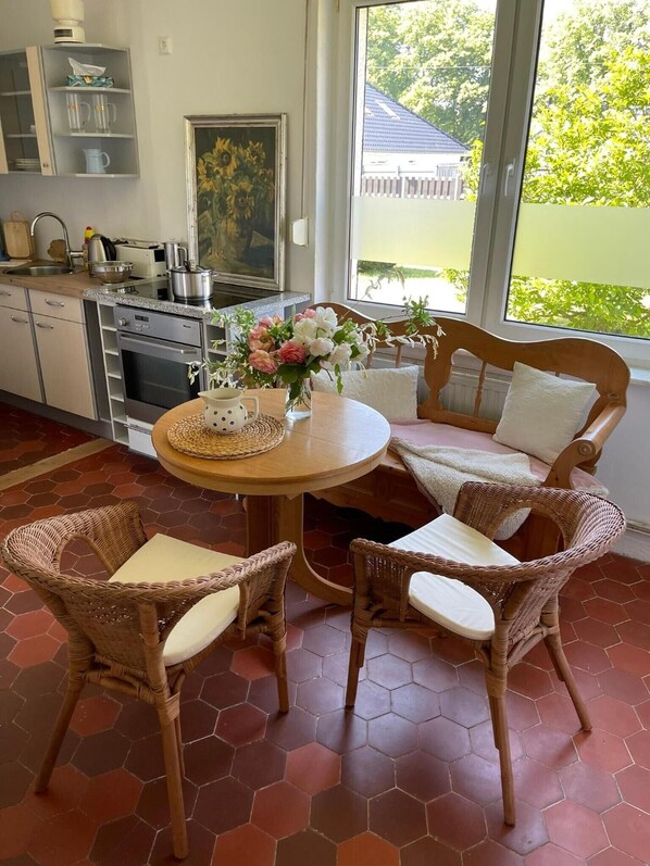 A kitchen with a dining area, including wicker chairs, a round table, and a view of the outdoors.