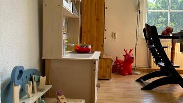 A room with a wooden table, a bookshelf, a window with a view of trees, and a red toy reindeer.