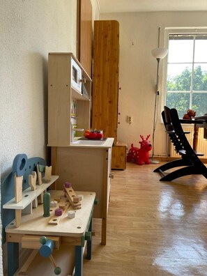 A room with a wooden table, a bookshelf, a window with a view of trees, and a red toy reindeer.