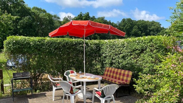Eine Terrasse im Freien mit Tisch, Stühlen, einem roten Sonnenschirm und einer Bank.