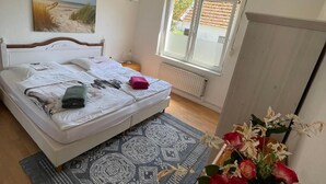 Ein Schlafzimmer mit Bett, Fenster, Heizkörper, Teppich und einer Blumenvase.