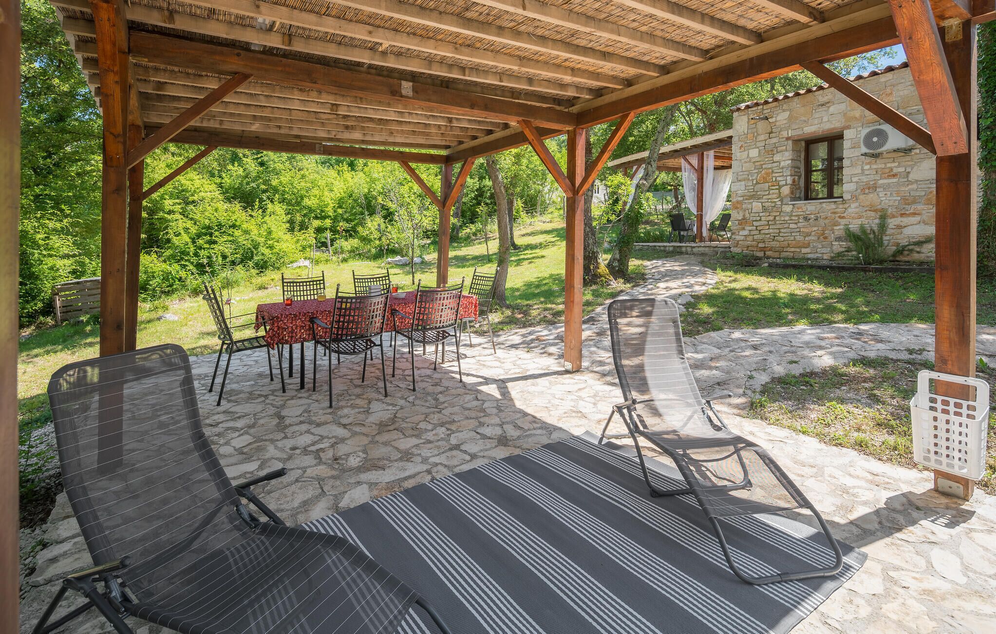 A covered outdoor seating area with stone flooring, metal chairs, and a table set for dining.