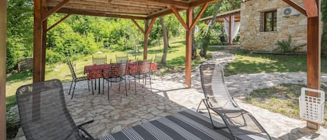 A covered outdoor seating area with stone flooring, metal chairs, and a table set for dining.