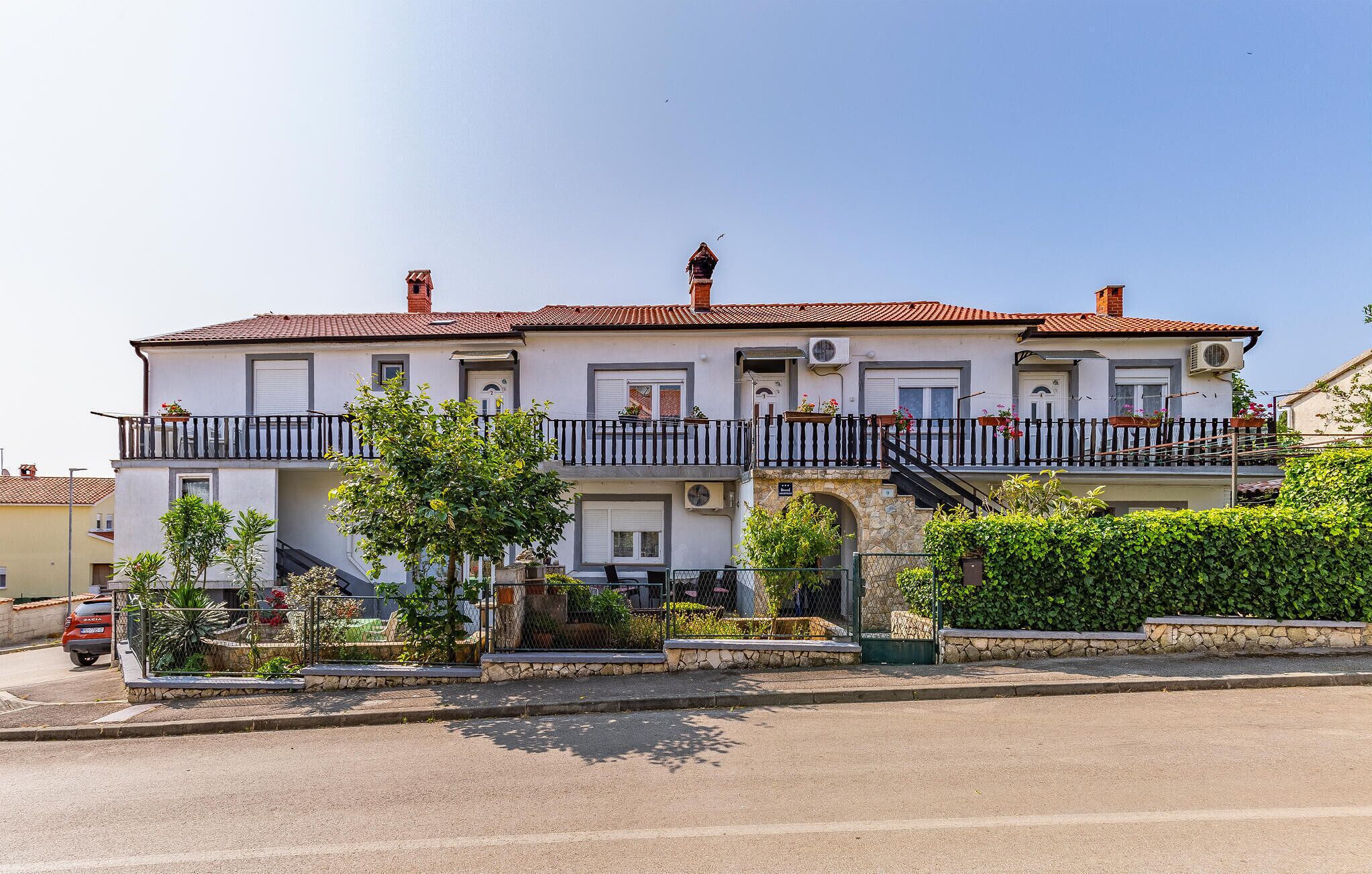 A two-story building with a balcony, a stone base, and a red-tiled roof.