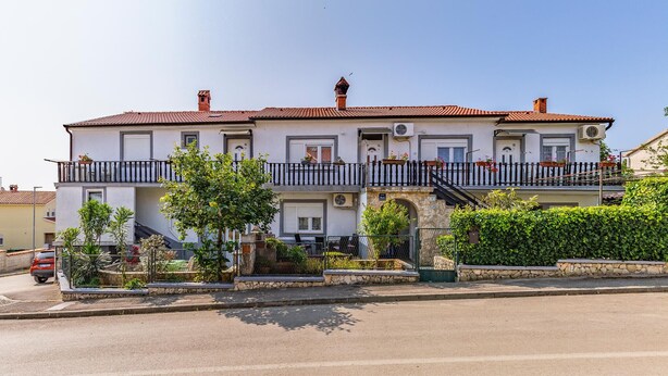 Ein zweistöckiges Gebäude mit einem Balkon, einem Steinunterbau und einem roten Ziegeldach.