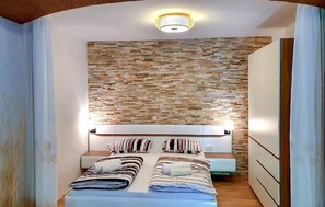 A bedroom with a stone wall, a bed with striped bedding, and a bedside table. - Awesome apartment in Dramalj with WiFi (Dramalj)