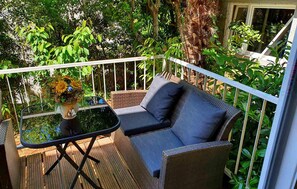 A balcony with wicker furniture, a small table with a vase of flowers, and lush greenery in the background. - Awesome apartment in Dramalj with WiFi (Dramalj)