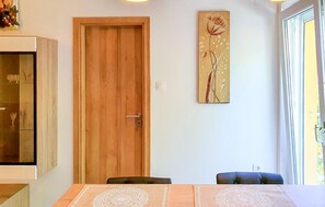 Une pièce avec une porte en bois, une table à manger avec un set de table, une chaise et une œuvre d’art accrochée au mur.