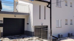 A two-story building with a tiled patio, a garage door, and a small balcony with a metal railing. - Beautiful apartment in Crikvenica with WiFi (Crikvenica)