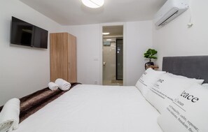 A modern hotel room with a bed, a TV, a wardrobe, and a small plant. - Beautiful apartment in Crikvenica with WiFi (Crikvenica)