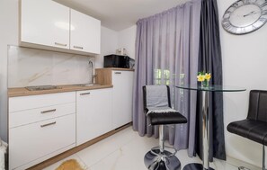 A modern kitchen with white cabinets, a marble countertop, a sink, and a black appliance. There is a glass table with a chair and a clock on the wall. - Beautiful apartment in Crikvenica with WiFi (Crikvenica)