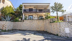 A two-story residential building with a stone wall in front, a balcony on the upper floor, and a clear sky. - Beautiful apartment in Crikvenica with WiFi (Crikvenica)