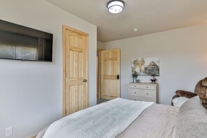 A bedroom with a bed, a dresser, a television mounted on the wall, and a door leading to another room. - Country Corner Inn - 3BR Stay for Professionals (Wausau)