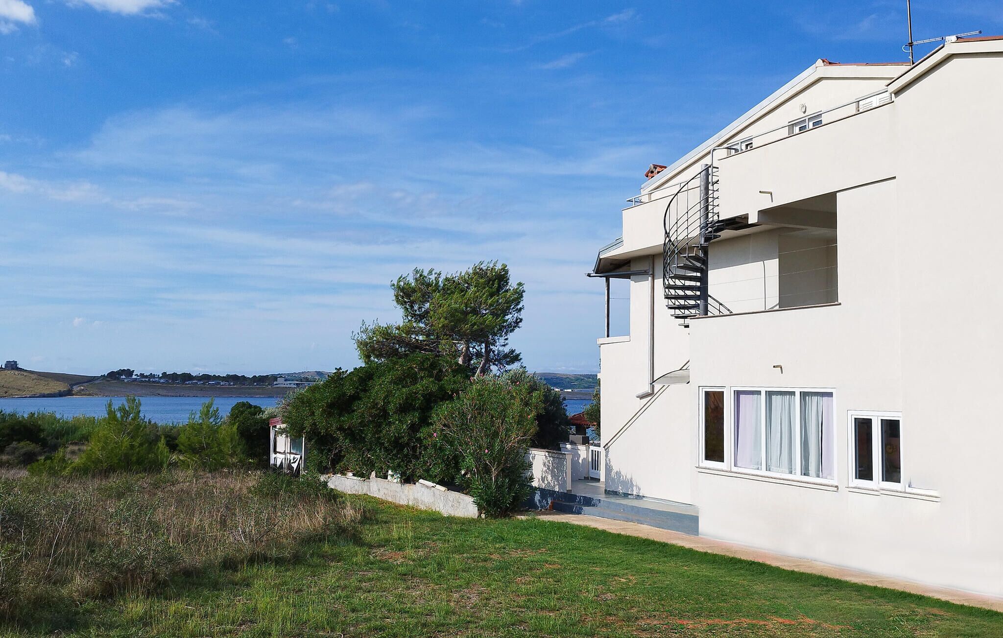 Ein modernes, zweistöckiges Gebäude mit weißer Fassade, einer sichtbaren Treppe und Blick aufs Meer.