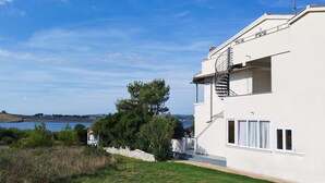 Ein modernes, zweistöckiges Gebäude mit weißer Fassade, einer sichtbaren Treppe und Blick aufs Meer.