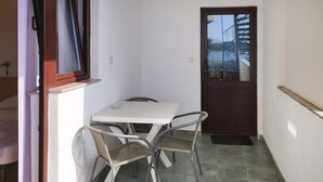 Ein kleiner, abgeschlossener Essbereich im Freien mit Tisch und zwei Stühlen, einer Tür und einem Fenster.