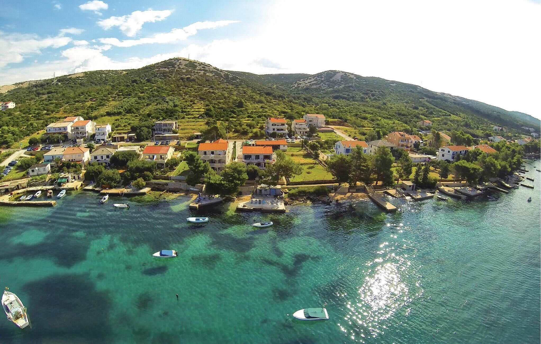 Vista aérea de un pueblo costero con casas, aguas turquesas cristalinas y barcos.