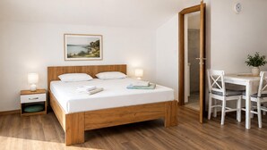 Ein Schlafzimmer mit einem hölzernen Bett, Nachttischen, einem Schreibtisch mit Stühlen und Meerblick.
