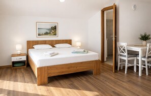 A bedroom with a wooden bed, bedside tables, a desk with chairs, and a view of the sea. - Stunning apartment in Smokvica with WiFi (Smokvica)