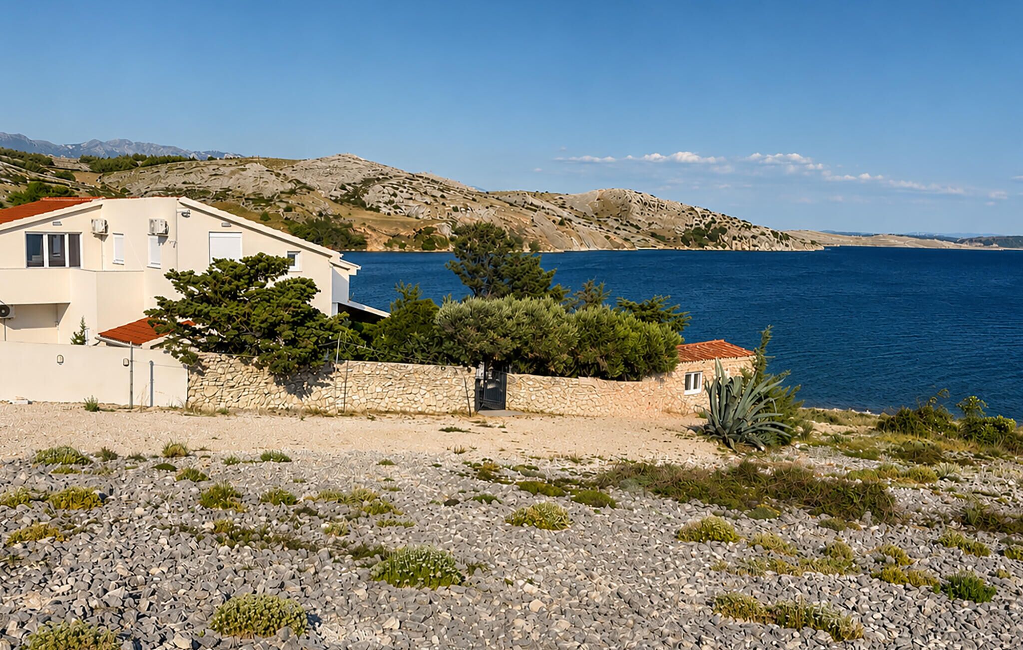 A coastal property with a white building, a stone wall, and a view of the sea.