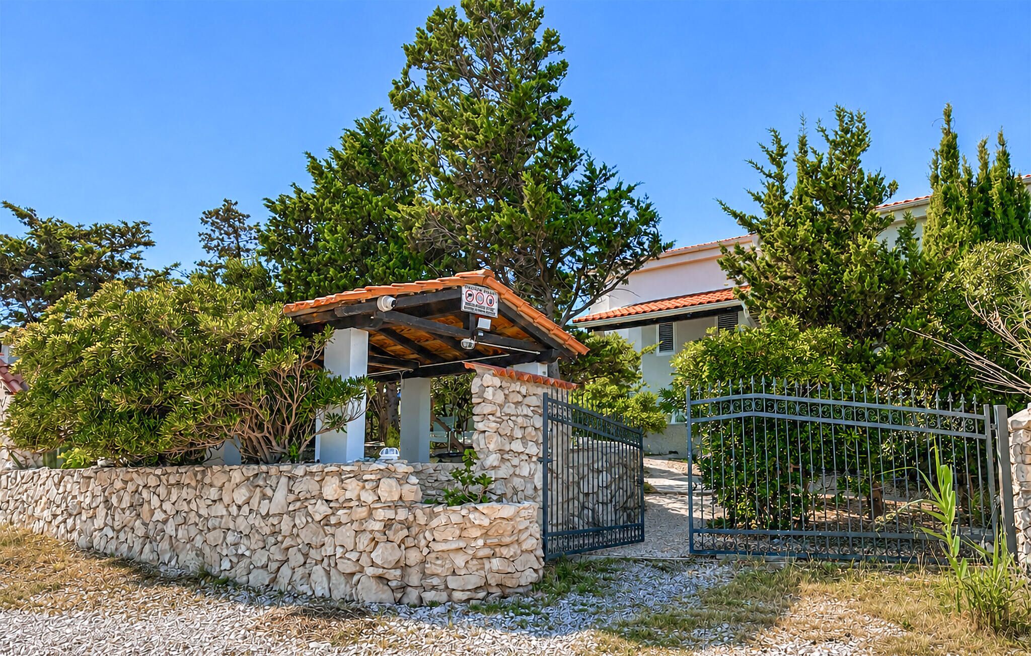 A stone wall with a covered structure, a metal gate, and a building with a red roof.