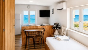 A compact room with a wooden table and chairs, a bed, a TV, and a window with a view of the sea. - Stunning apartment in Smokvica (Smokvica)
