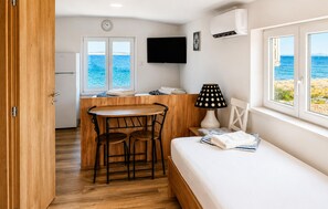 Ein kleines Zimmer mit Holztisch und -stühlen, einem Bett, einem Fernseher und einem Fenster mit Meerblick.
