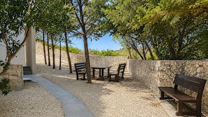 An outdoor seating area with a stone wall, a concrete pathway, and trees. - Stunning apartment in Smokvica (Smokvica)
