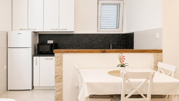 Uma cozinha compacta com armários brancos, bancada preta, micro-ondas e geladeira.