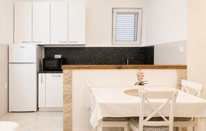 A compact kitchen with white cabinets, a black countertop, a microwave, and a refrigerator. - Nice apartment in Smokvica with WiFi (Smokvica)