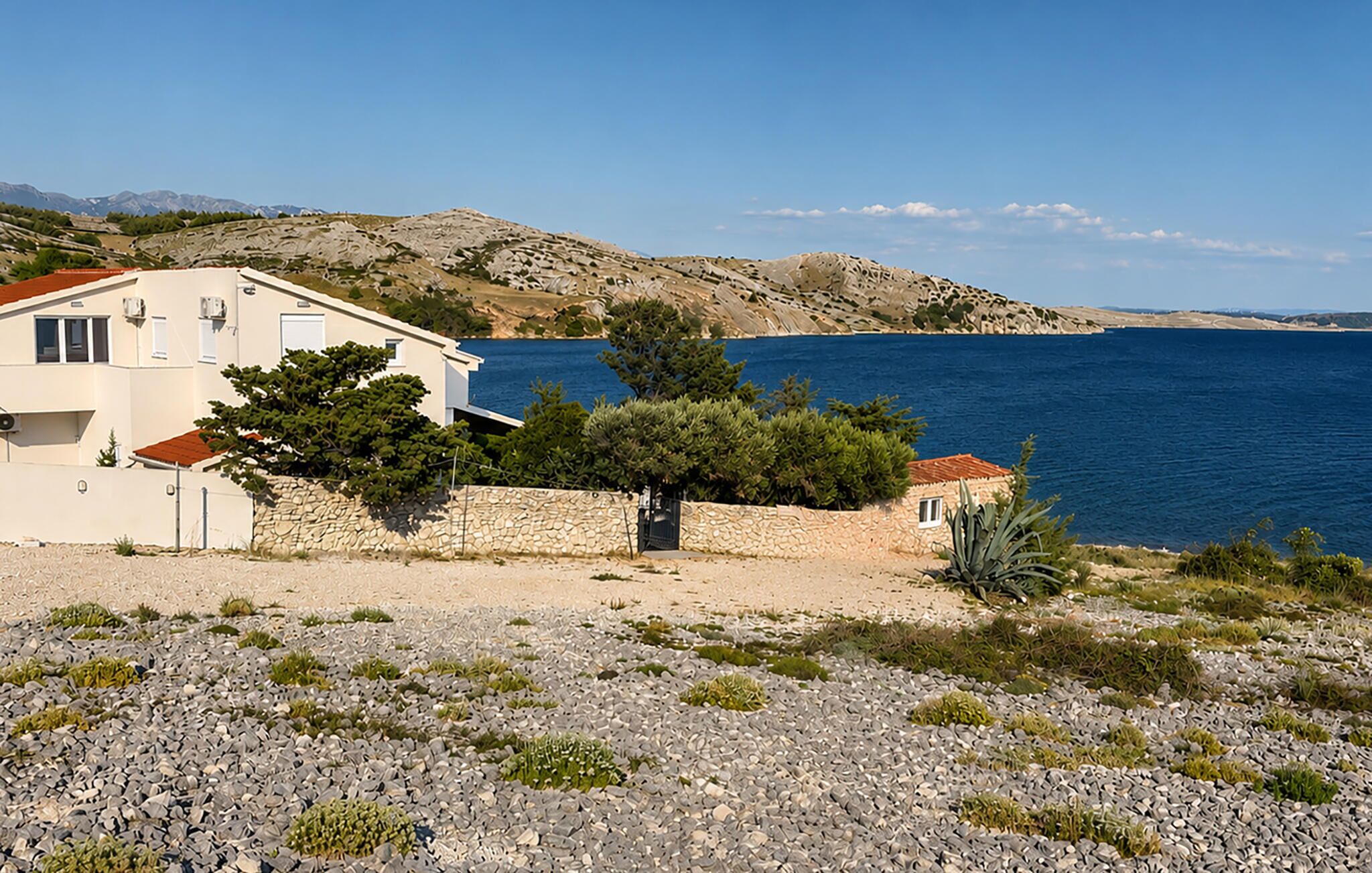 A coastal property with a stone wall, a white building with a red roof, and a view of the sea.