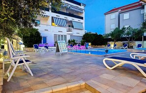 A pool area with lounge chairs, a signboard, and a building with balconies. - Apartment in Stara Novalja (139) (Stara Novalja)