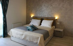 A neatly made bed with a textured blanket, two pillows, and a decorative pillow. There are two bedside tables with lamps. The room has a simple, clean design with a light-colored floor and a plain wall. - Apartment in Stara Novalja (139) (Stara Novalja)