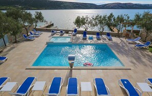 Ein Poolbereich mit mehreren Liegestühlen und einem zentralen Schwimmbecken, umgeben von Bäumen und Blick auf einen See.