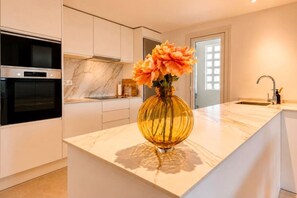 A modern kitchen with a marble countertop, a built-in oven, and a vase with flowers on the island. - Luxury new apartment in La Cala de Mijas (Las Lagunas de Mijas)