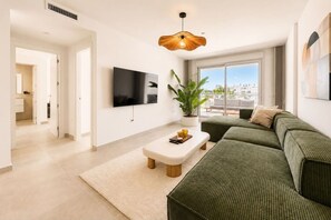 A modern living room with a flat-screen TV, a green sofa set, a coffee table, and a potted plant. - Luxury new apartment in La Cala de Mijas (Las Lagunas de Mijas)