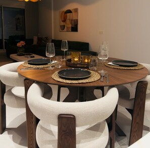 Une table de salle à manger ronde, avec des assiettes noires, des verres transparents et un set de table en fibres tressées.