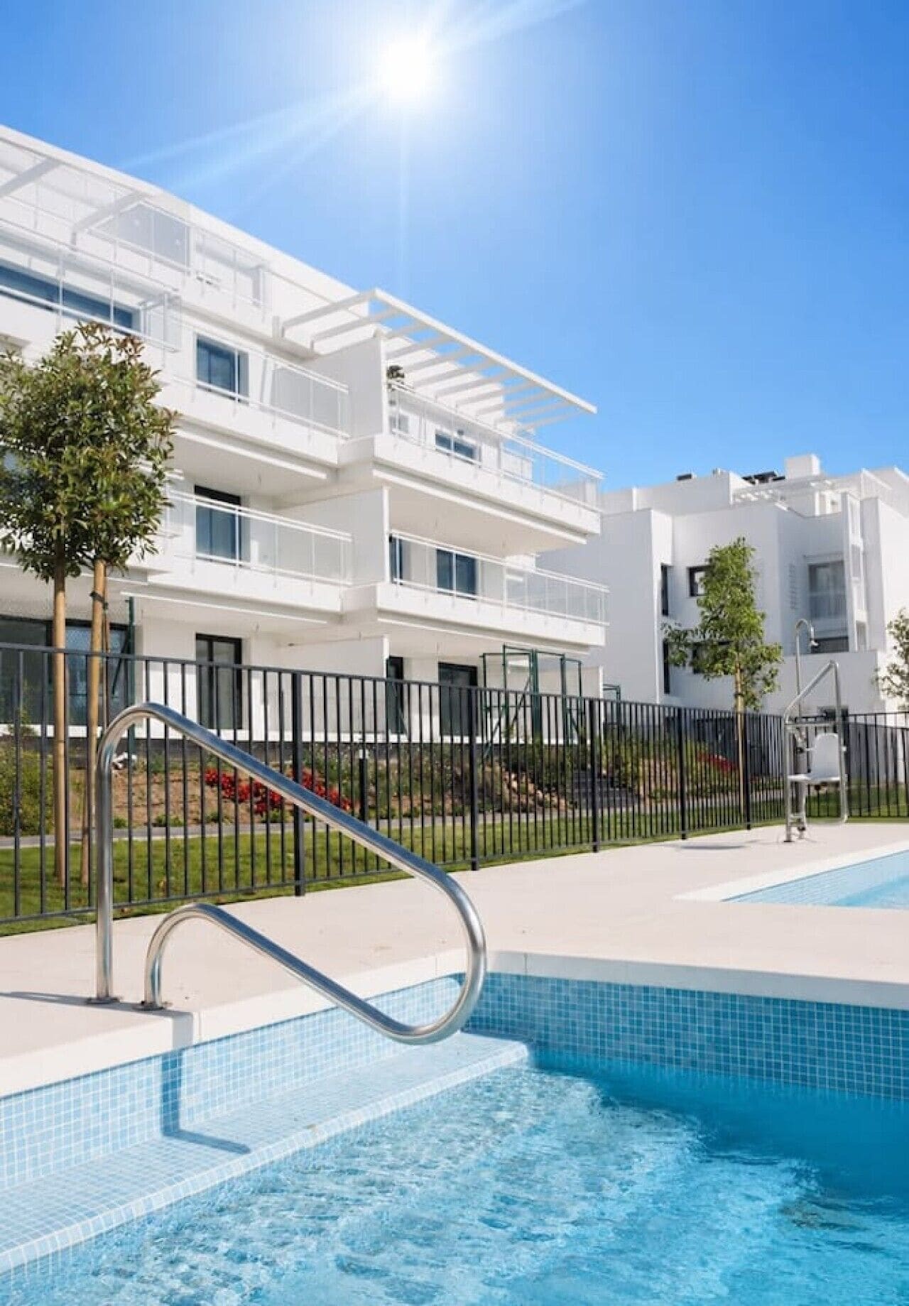A modern apartment building with a swimming pool and a metal staircase leading into the pool.