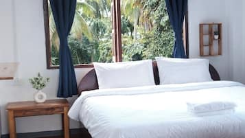 A bedroom with a bed, a bedside table with a plant, a window with curtains, and an air conditioning unit.