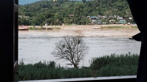 Vista dall'interno di un veicolo, su un fiume con una grande statua dorata su una collina in lontananza.