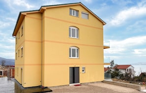 Ein gelbes, mehrstöckiges Gebäude mit flachem Dach, einem kleinen Balkon und einer Tür mit roter Fußmatte.