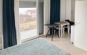 Ein Zimmer mit einem Bett, einem Tisch, einem Stuhl, einer Glastür und Blick auf Gebäude.