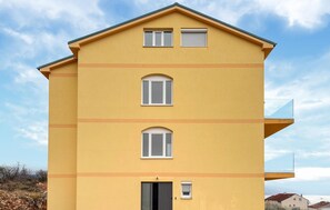 Een geel meerlaags gebouw met drie ramen per verdieping, een balkon aan de rechterkant en een deur onderaan.