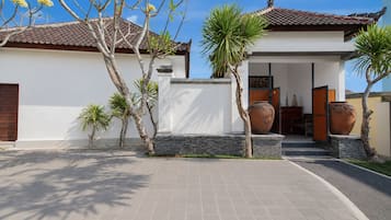 A modern house with a tiled roof, a paved driveway, and a small garden with palm trees and a large pot.