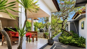 A covered outdoor area with a dining table, chairs, and a bench. There are potted plants and a pathway leading to a building entrance. - Collection O near Pantai Nusadua formerl (Nusa Dua)