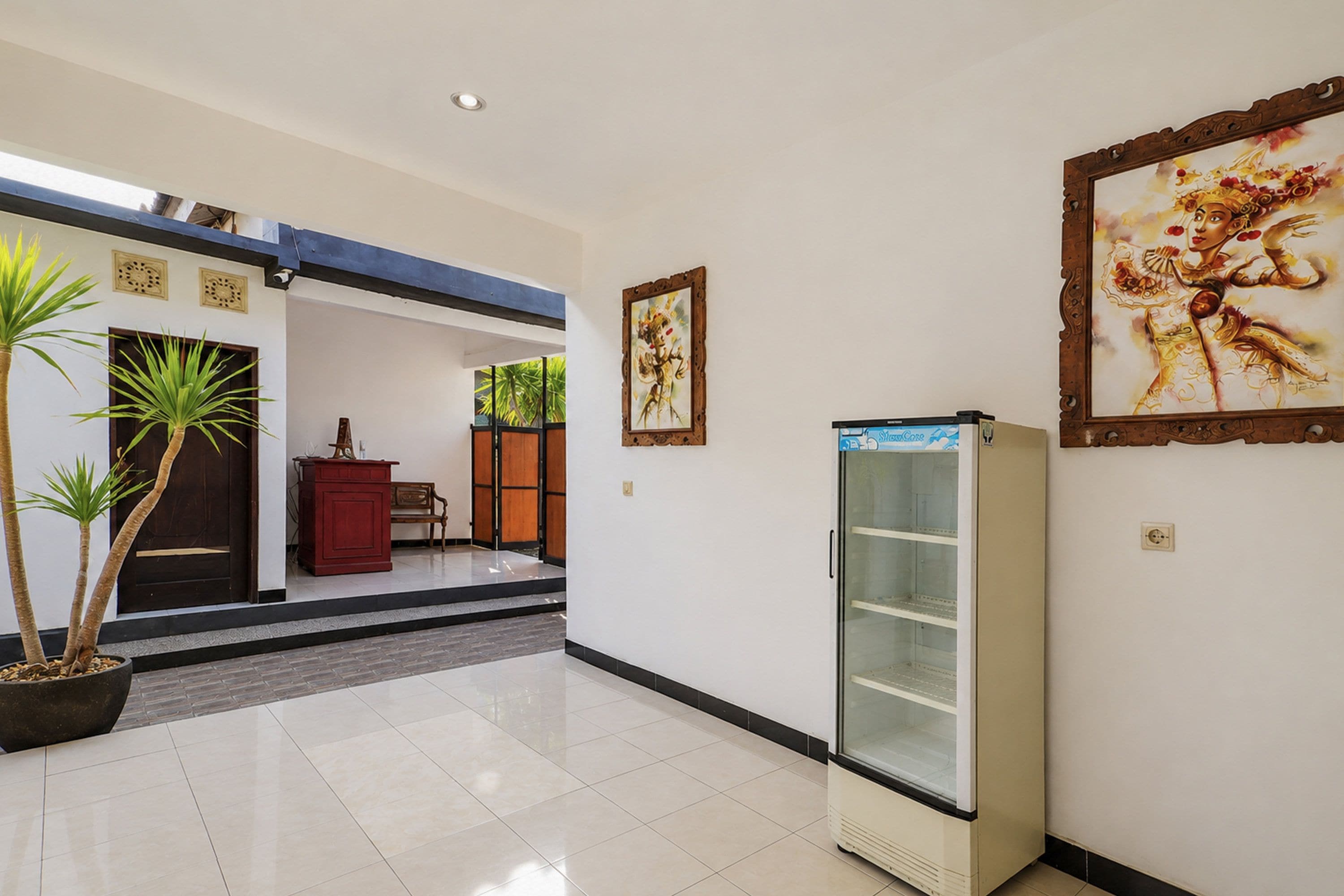 A hallway with a refrigerator, a bench, and a door leading to another room.